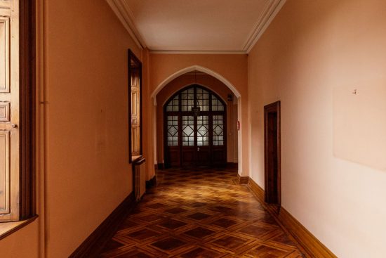 A hallway with parquet floor and several windows with seats ends at a beautiful window with exquisite decorative millwork.