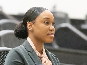 A student in a business suit sitting in a classroom looking at the front of the room.