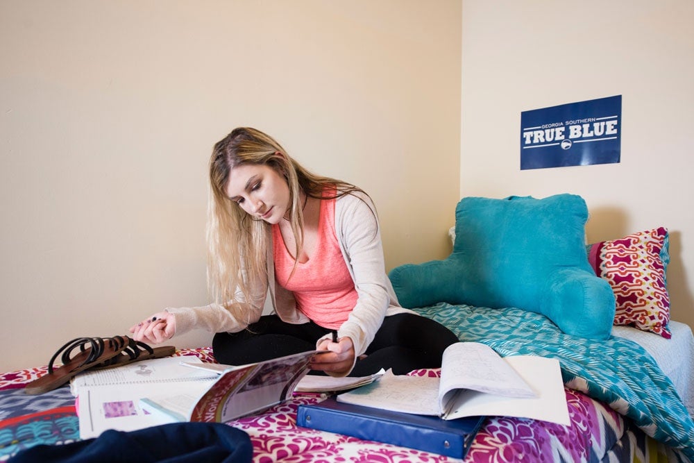 A student reads textbooks from her bed in a Georgia Southern dorm room