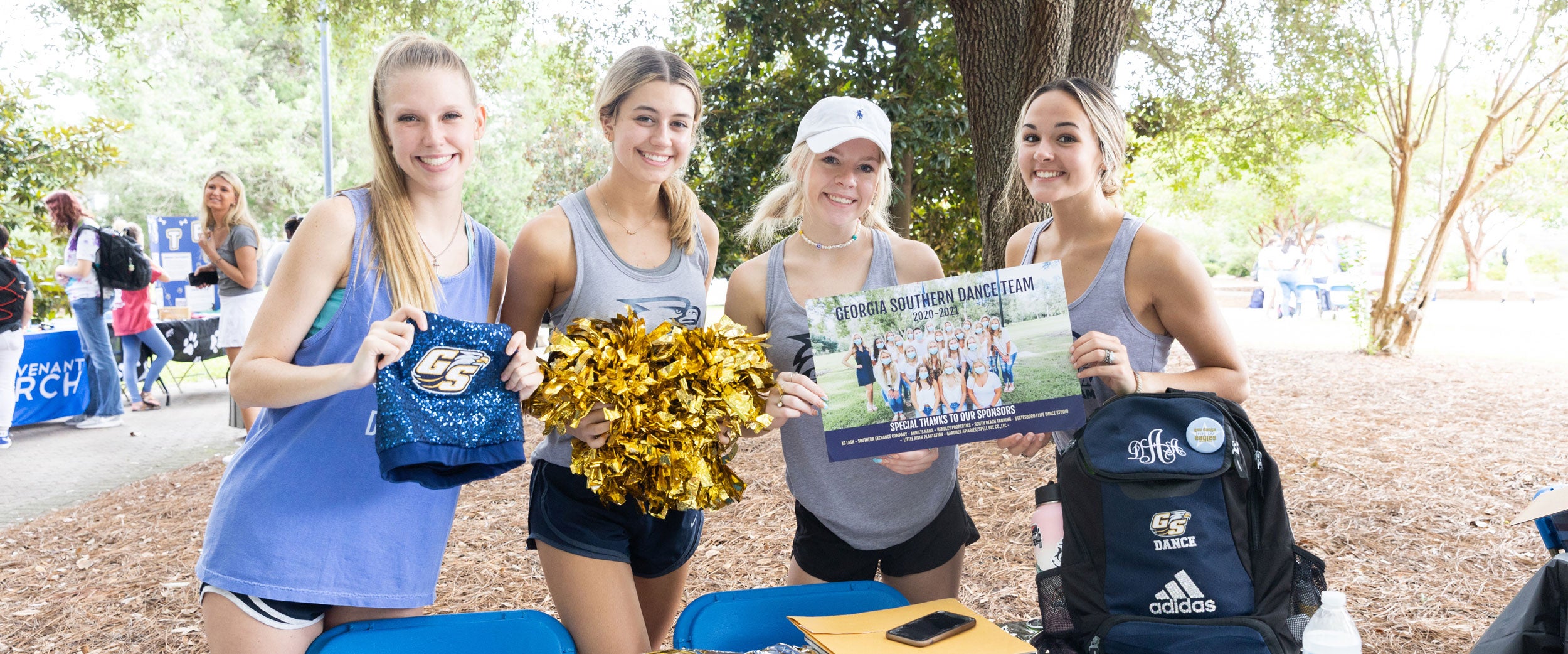 Four students promote Georgia Southern's dance team with a poster and pom-poms