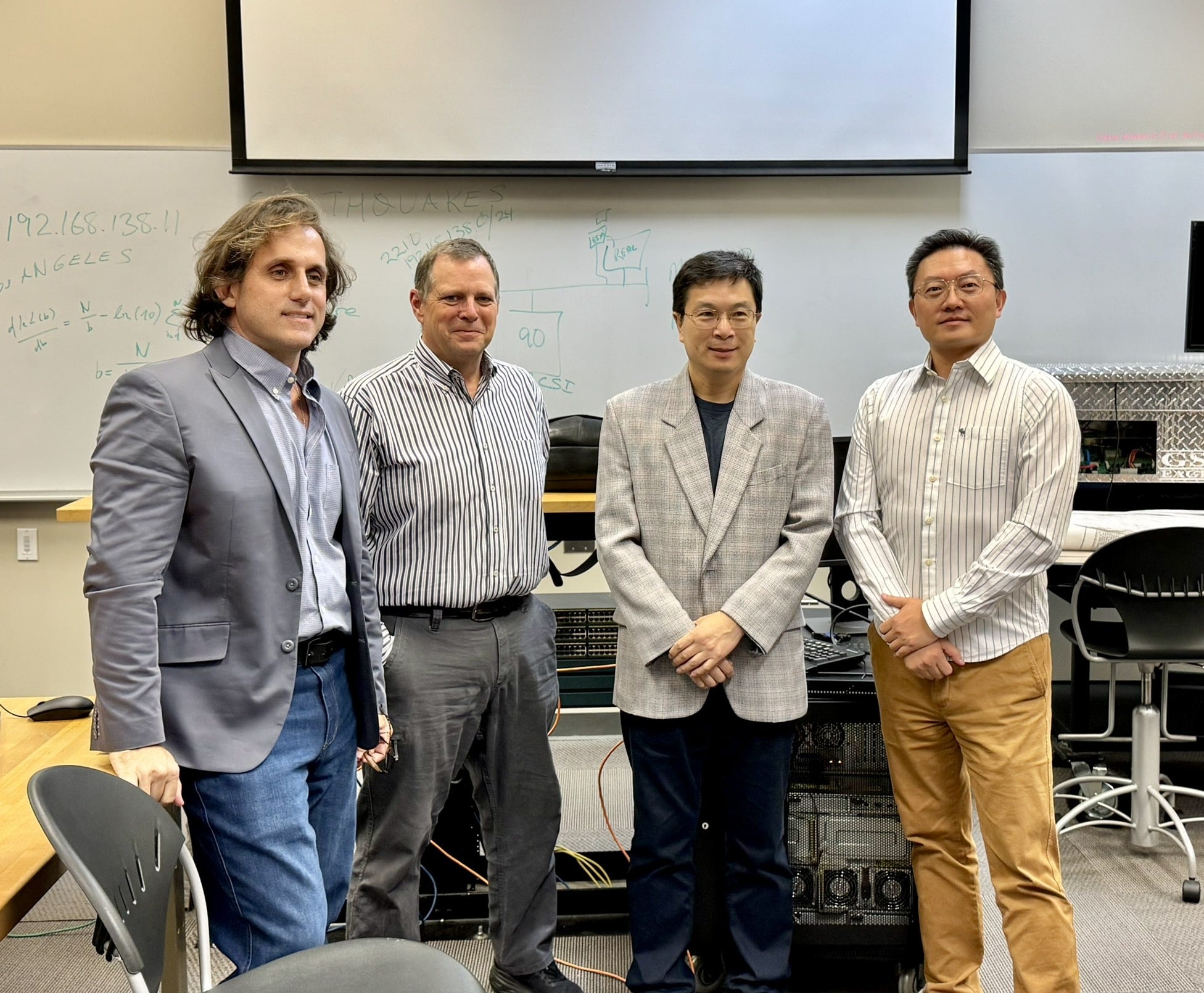 Four men stand in a classroom.