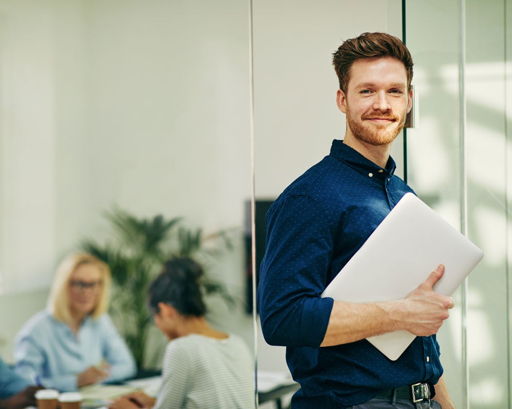 smiling young man standing with laptop