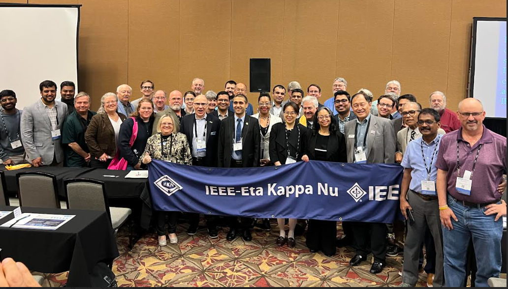 A large group of people gathered around a banner for IEEE Eta Kappa Nu.