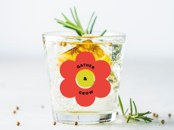 A glass of gin with the Gather and Grow logo and a sprig of juniper.