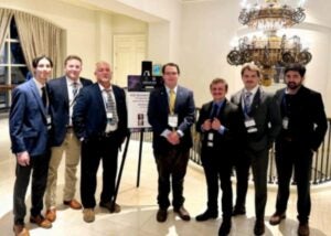 Seven men pose for a photo with a presentation board.