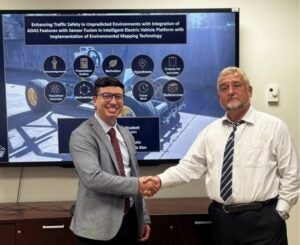 Two men shake hands with an engineering poster in the background.