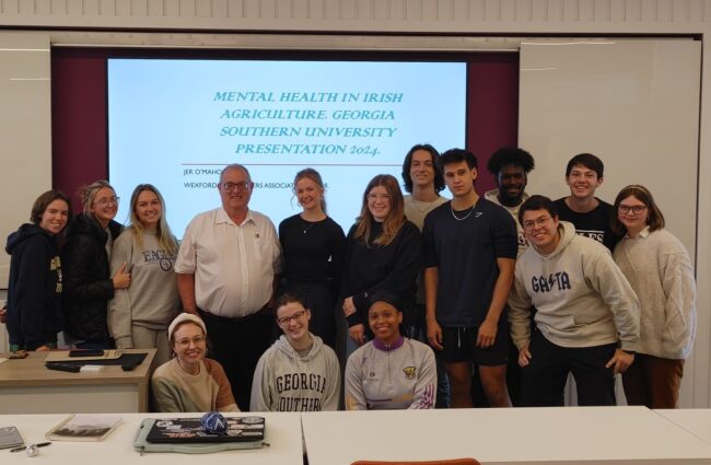Group of students and a lecturer posing in a classroom in front of a slide titled 'Mental Health in Irish Agriculture' for a Georgia Southern University presentation 2024.