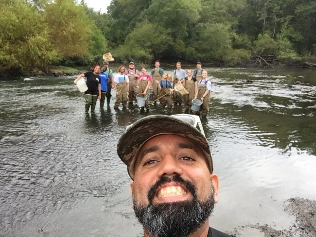Biology professor Checo Colón-Gaud, Ph.D., stands and poses with his students in a river.