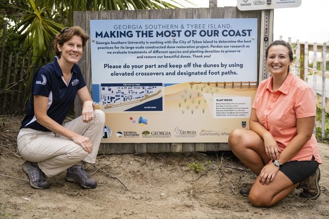 Shannon Matzke, right, poses for a picture with her advisor and Georgia Southern biology professor Lissa Leege, Ph.D., at a sign detailing her sand dune restoration project on Tybee Island.