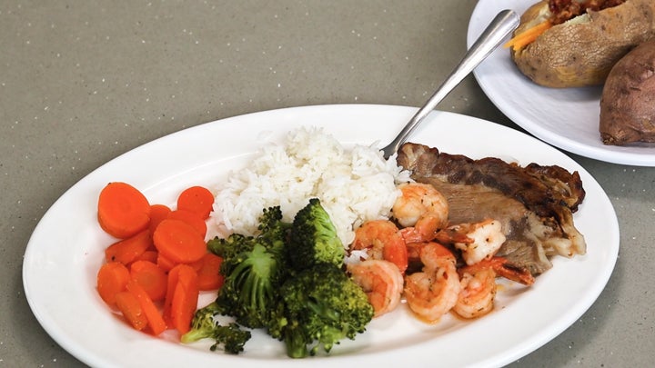 A just-like-home-cooked meal including cooked carrots, broccoli, grilled shrimp, roast beef and loaded baked potato.