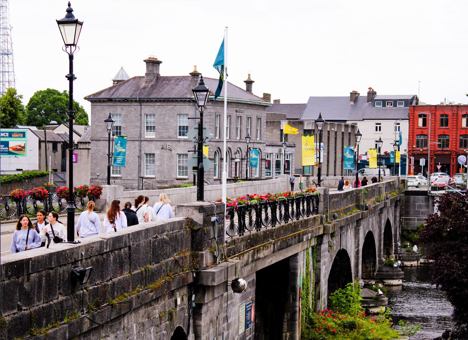 Beautiful cityscape with bright colored buildings featuring a bridge with flowers and greenery growing along the sides and water underneath.