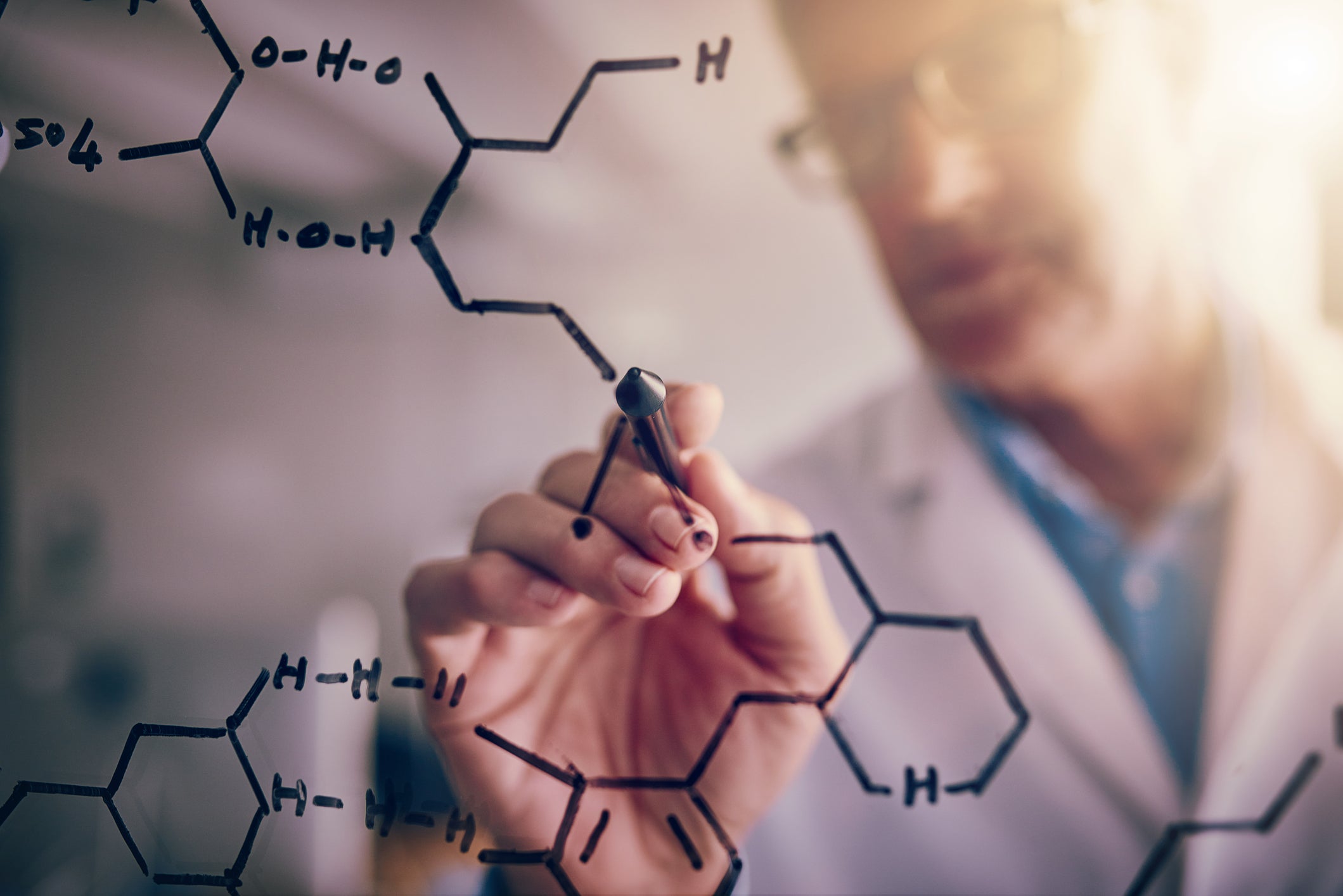 Doctor brainstorming by writing chemical formula on glass board with marker