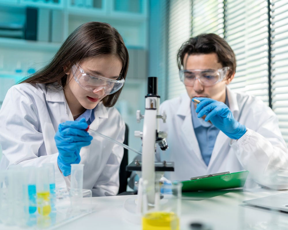 Two students working in a research science laboratory looking at a sample under a microscope.