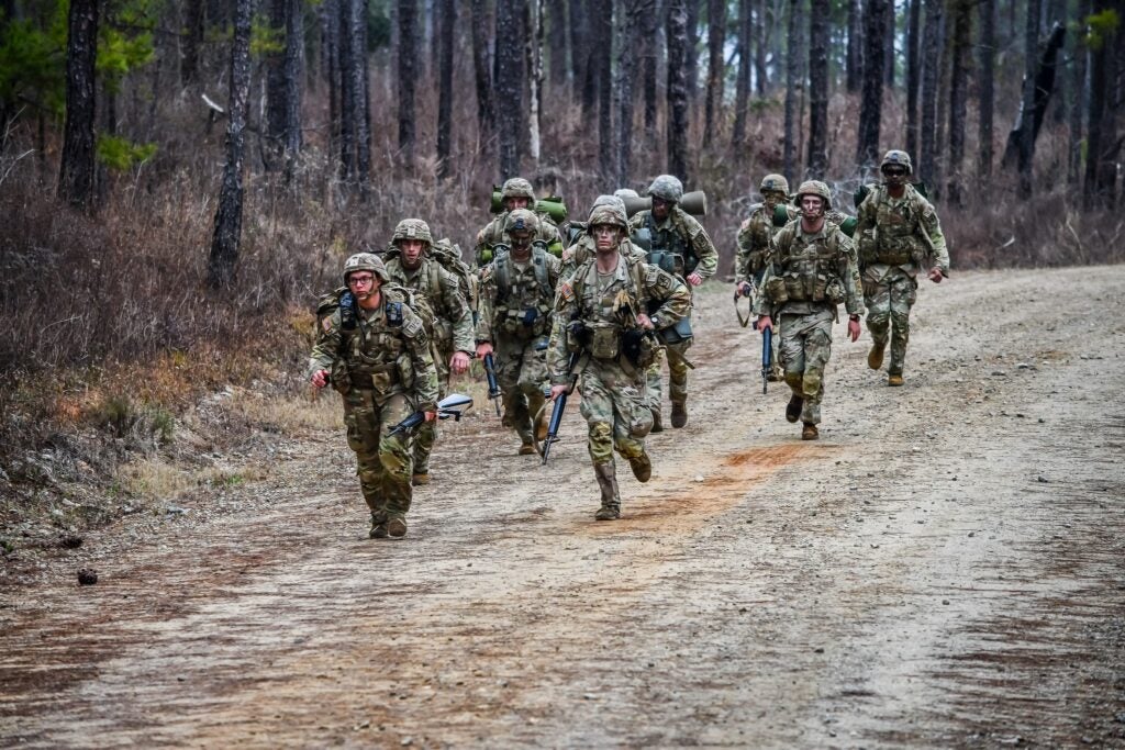 Georgia Southern Eagle Battalion running together in camouflage fatigues with black paint smudged on their faces on a dirt trail in the woods 