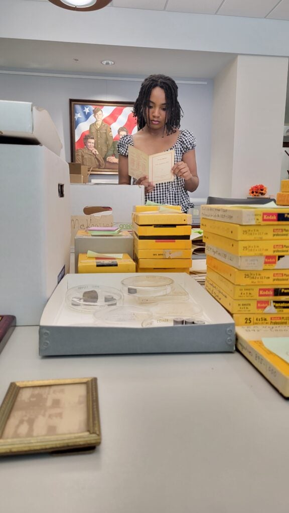 Ariana Taylor examines a document. Boxes of archive material are laid on a table in front of her.