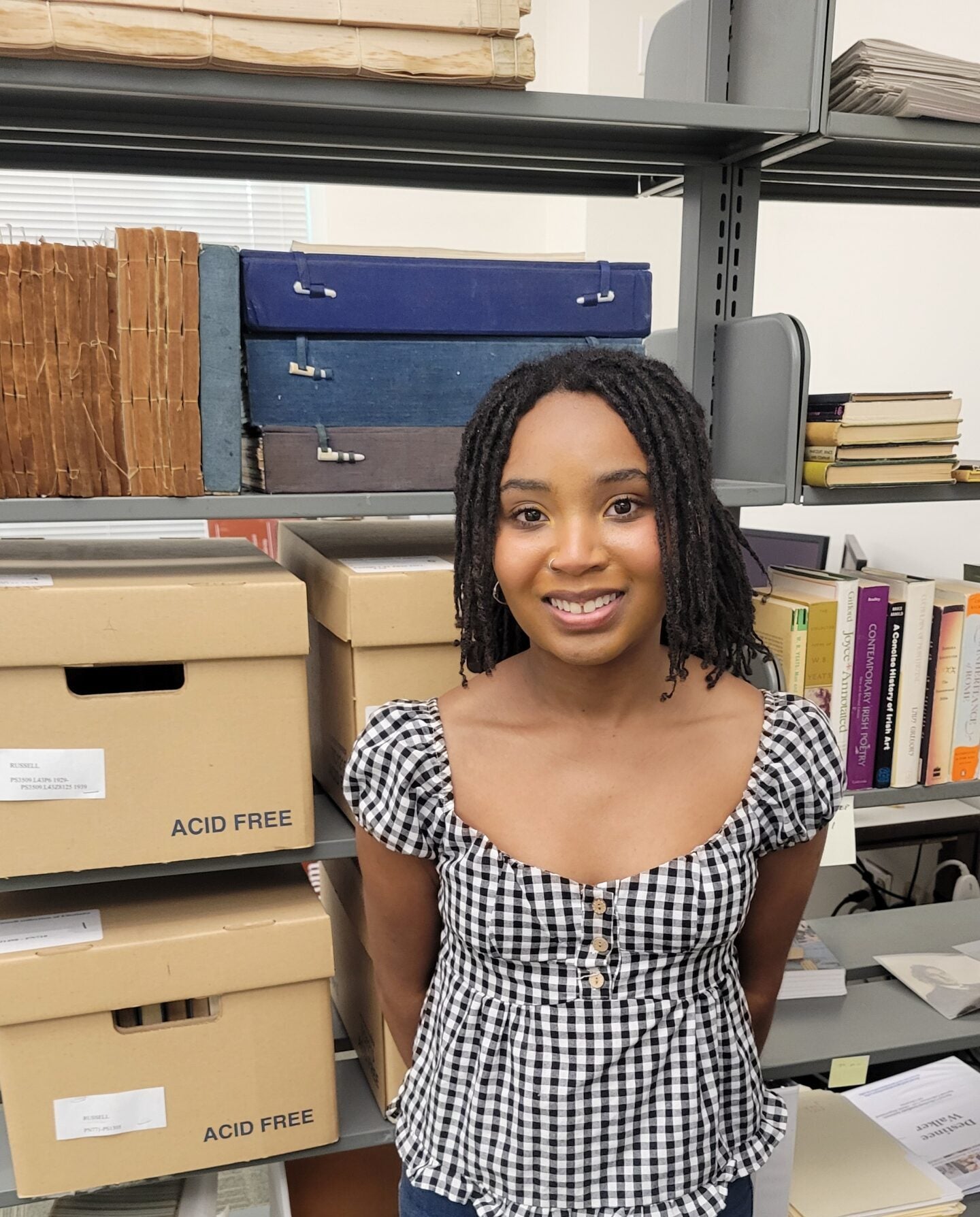 Ariana Taylor smiles while standing in front of shelves of archival material