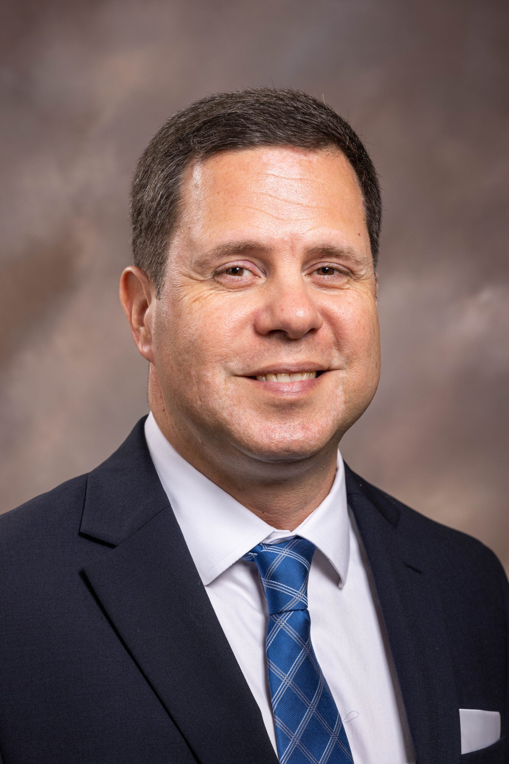 Joe Kardouni smiles while wearing a dark suit, white shirt and blue tie