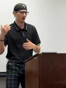Alexander Millstone stands at a lecture while debating