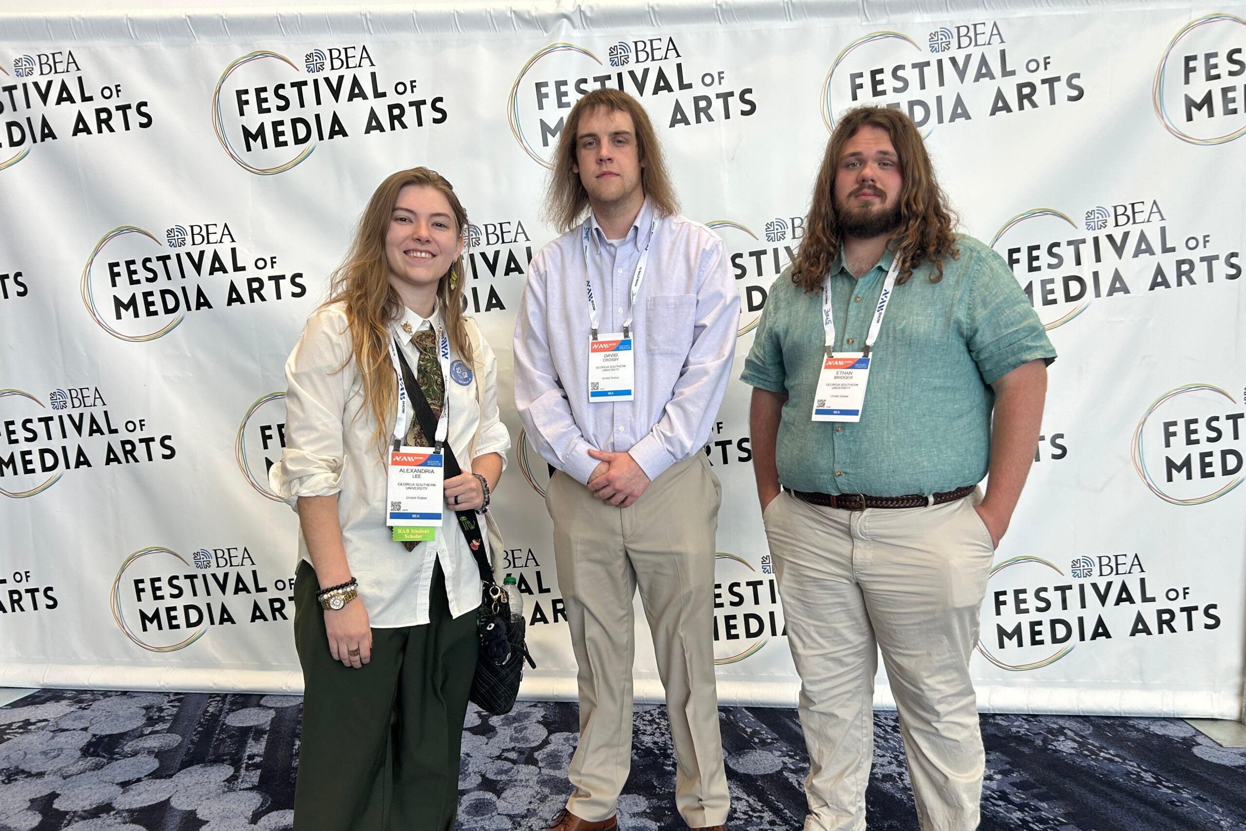 Three students stand in front of a banner that reads "Festival of Media Arts"