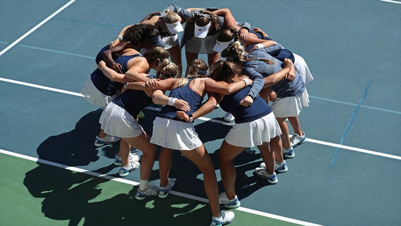 Women's tennis team huddled together on the court