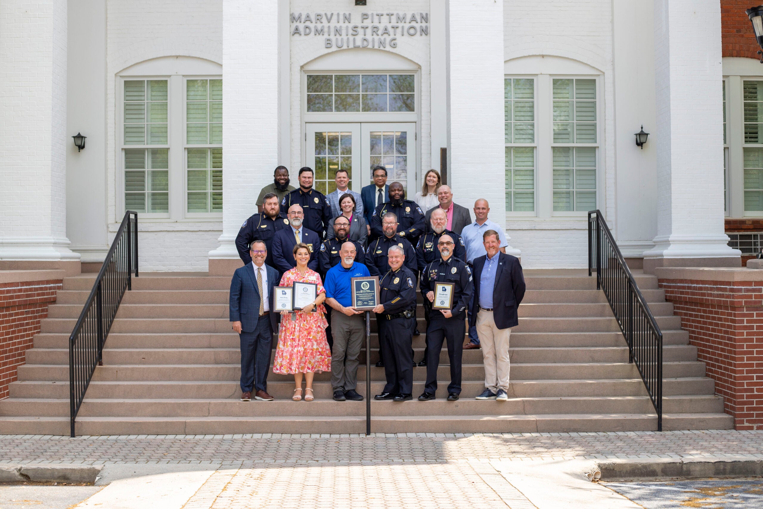 Members of Georgia Southern University leadership and the University Police Department stand on the steps of the Marvin Pittman Administration Building, smiling and holding plaques identifying multiple certifications and awards.