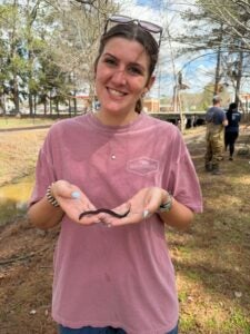 Lily Pavliscsak smiles while holding a small snake outdoors