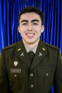Portrait of a young man in US Army dress greens, with name Coulter, smiling in front of a blue curtain.