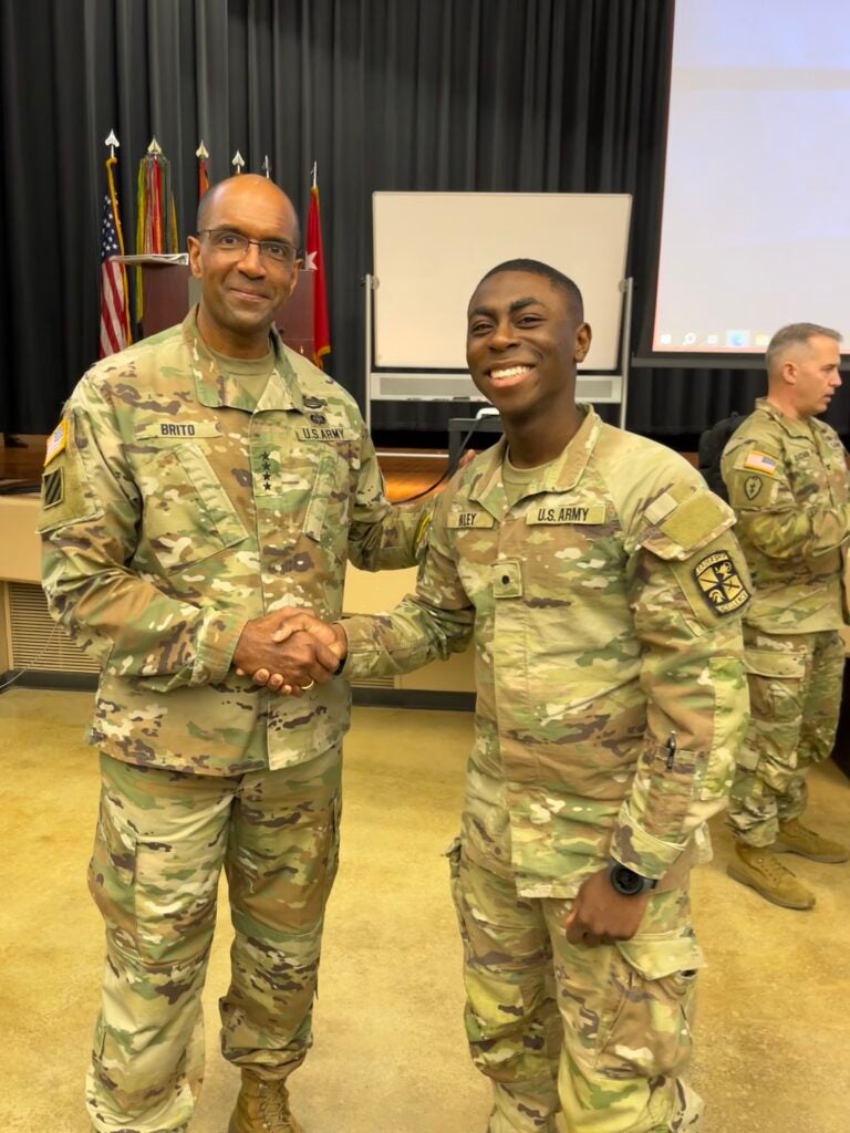 Two soldiers shake hands in front of a classroom, symbolizing camaraderie and cooperation in a learning environment.