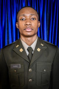 Portrait of a man in a U.S. Army dress uniform with a blue curtain backdrop; name tag reads THOMAS in the chest pocket.