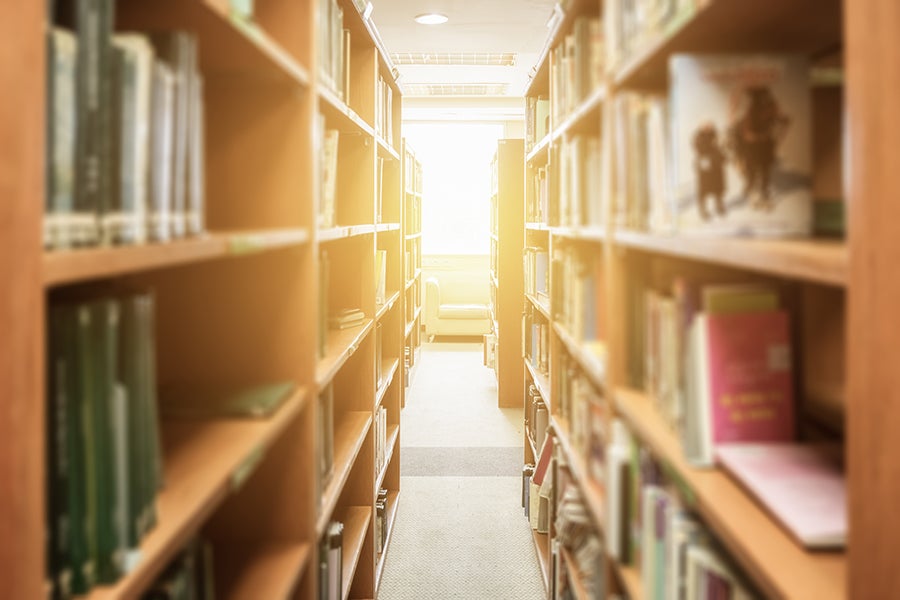 Narrow library aisle with tall wooden shelves full of books and bright light at the far end.