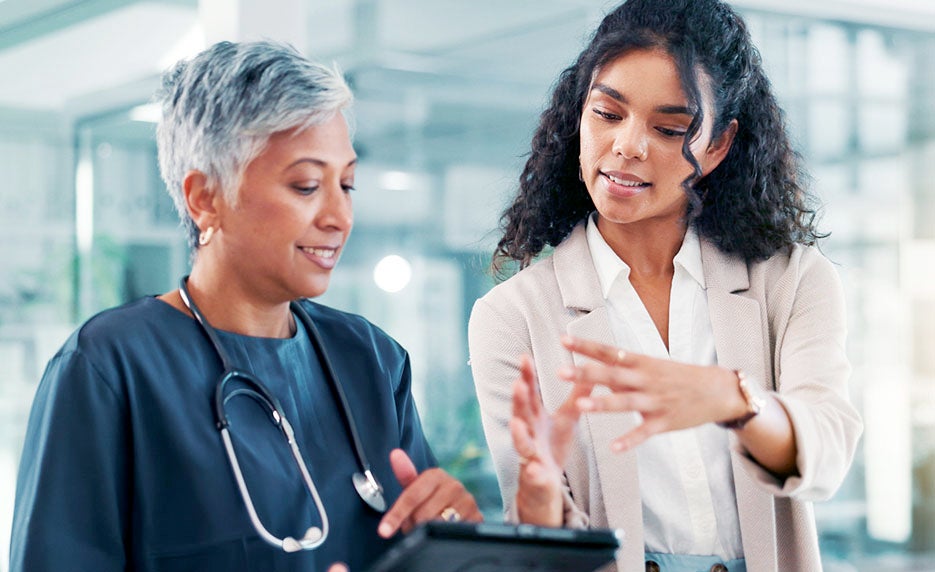 Two healthcare professionals review information on a tablet during a patient consultation in a bright clinic setting.