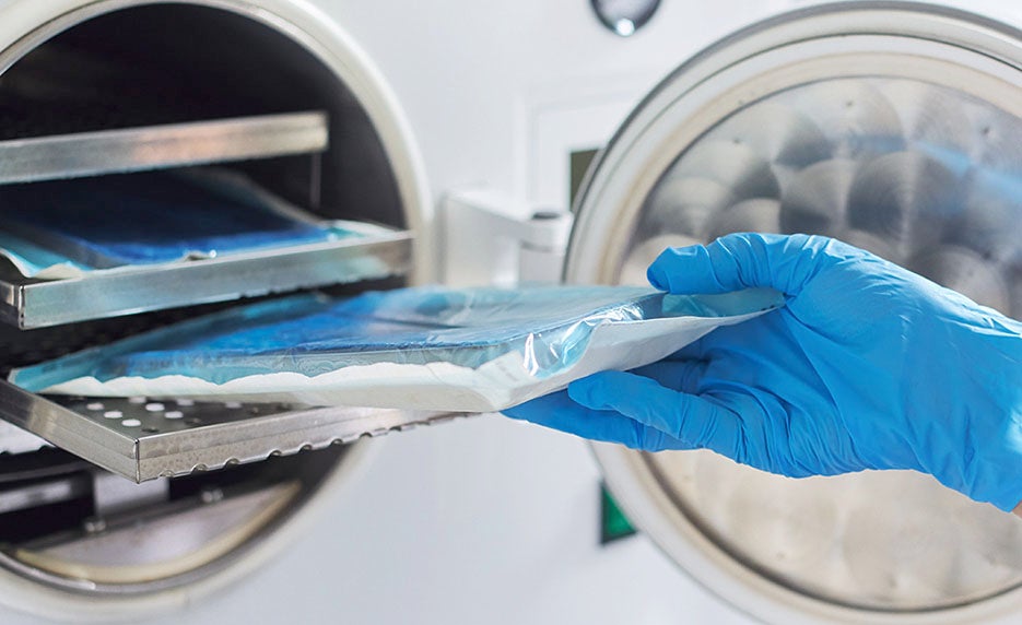 Gloved hand inserting a sealed medical sterilization pouch into an autoclave for sterilization.