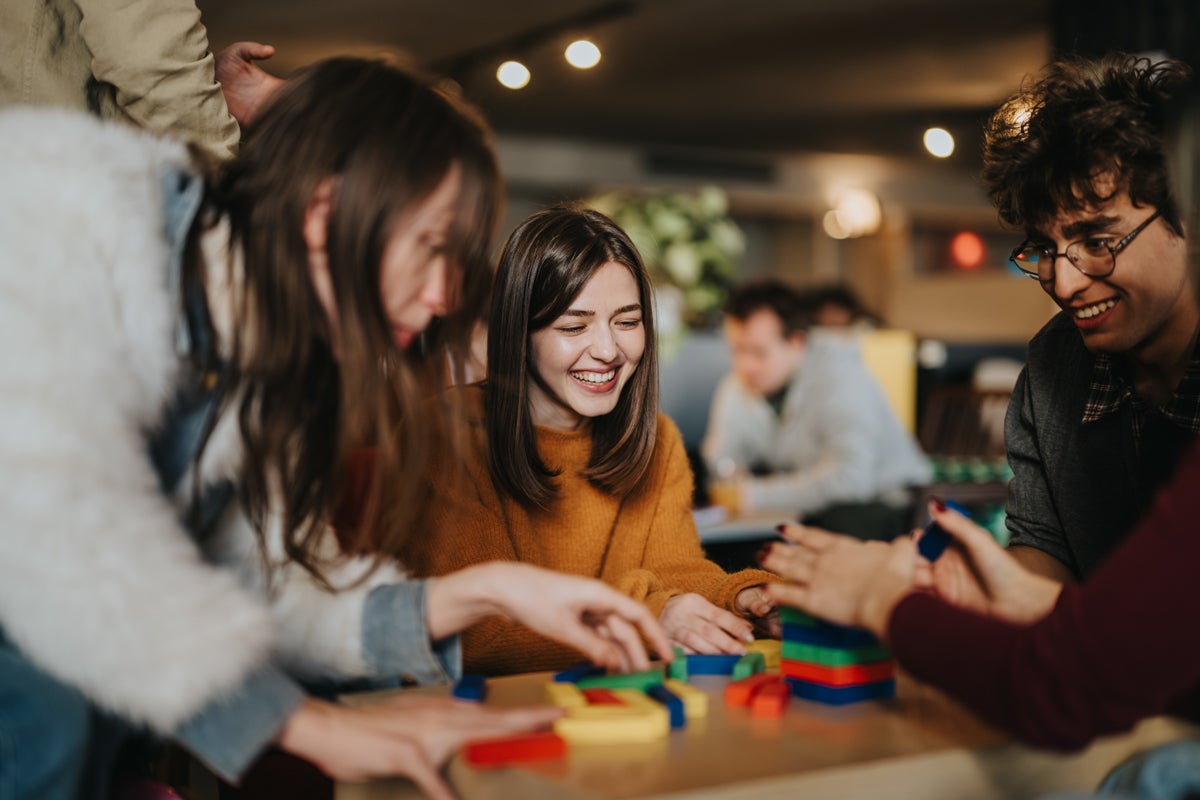 Group of young adults playing with colorful building blocks at a table, smiling and chatting.