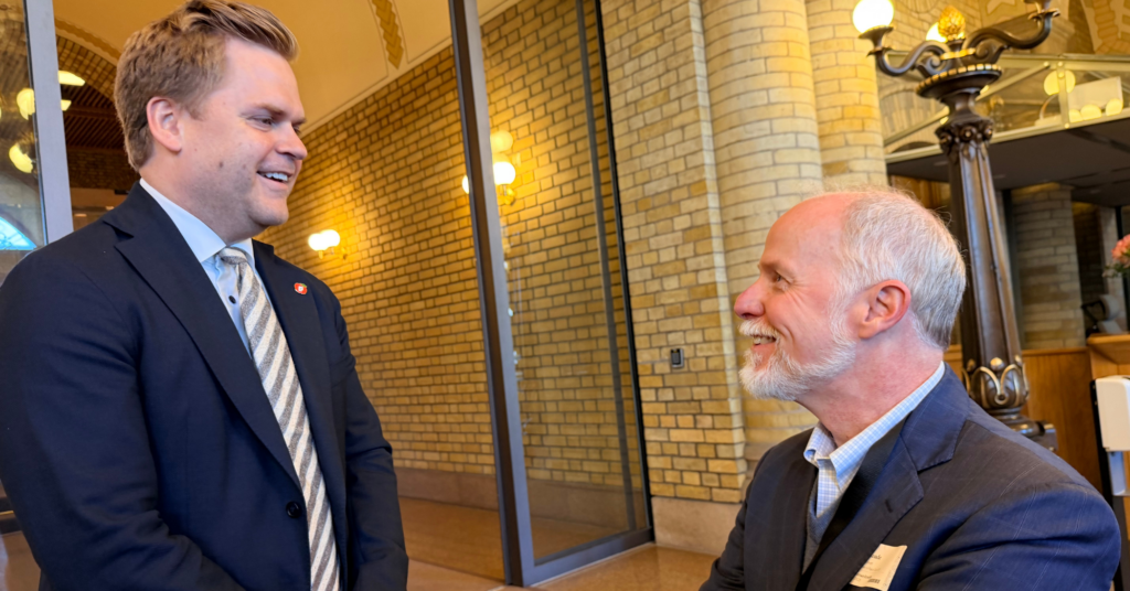 Two men in suits talk to each other in Oslo, Norway. They are both happy to be there. 