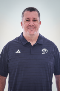 Jonathan Clasen smiling in a navy polo shirt with Adidas stripes on the left chest and a circular eagle emblem on the right, against a light background