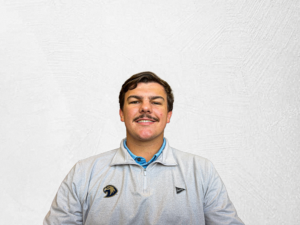 Justin Gray Smiling in a light gray zip-up jacket against a white textured wall.