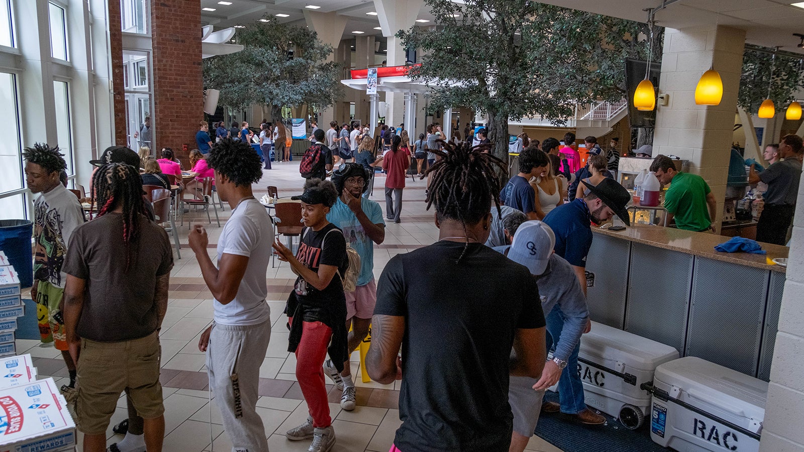 Crowded campus cafeteria or student center with a long service counter and students waiting in line.