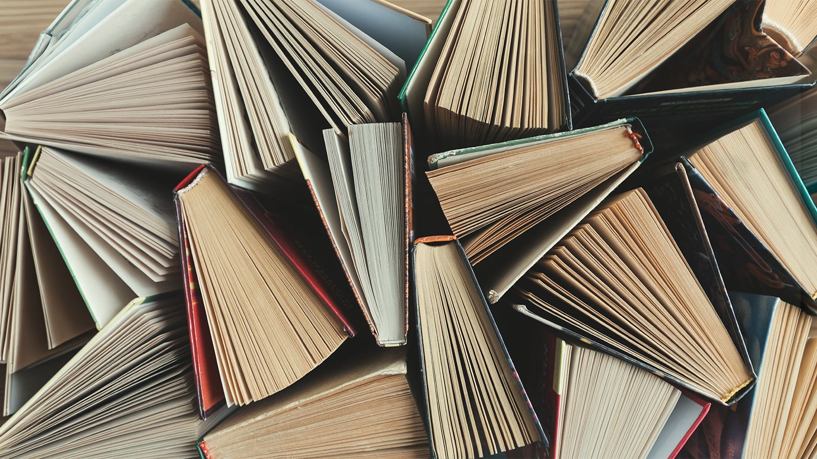 Aerial view of a clutter of open and closed books stacked together on a wooden surface.