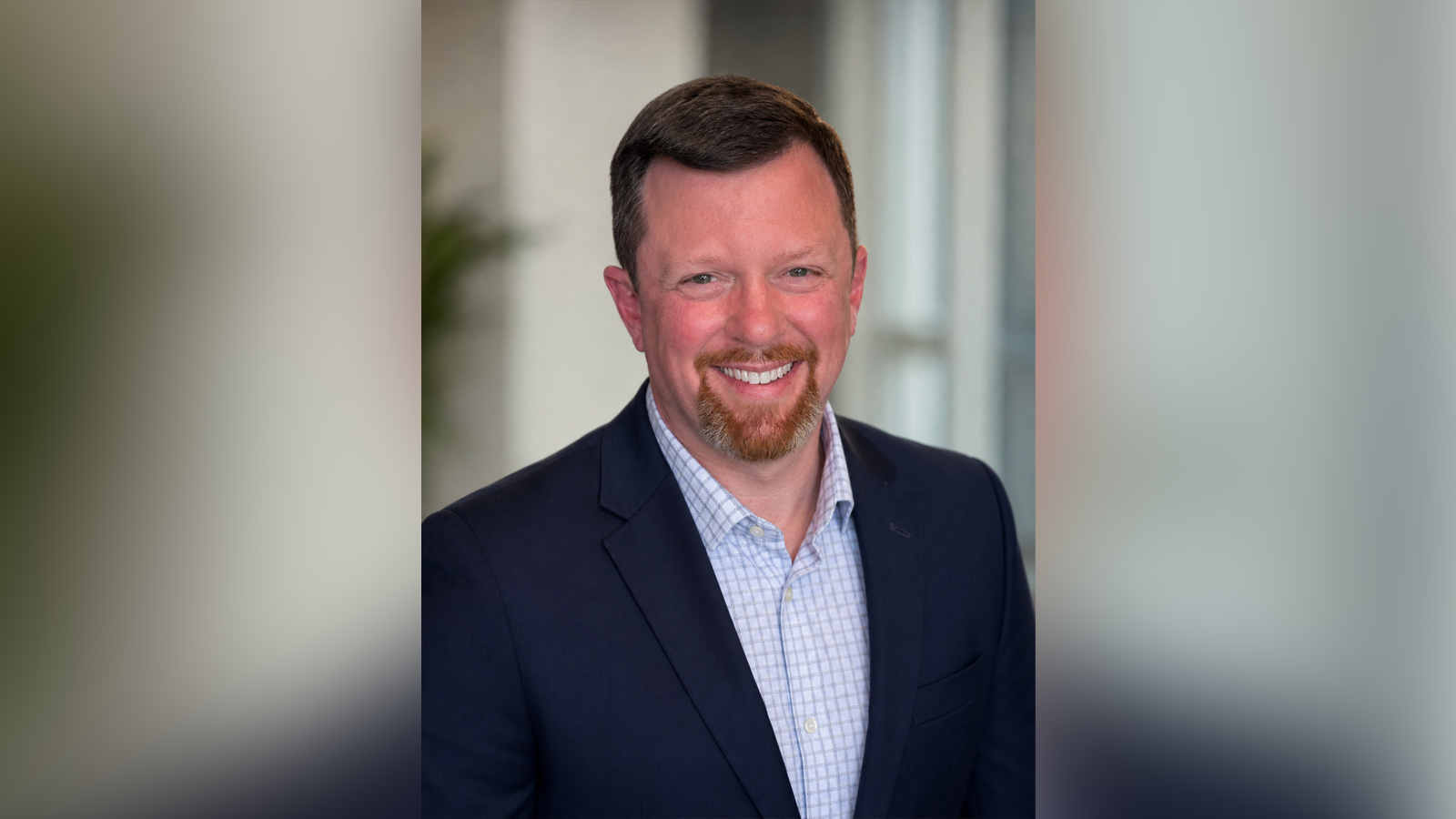 Smiling man in a navy blazer and light blue check shirt—professional headshot.