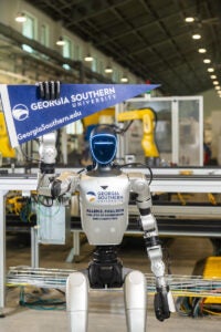 Humanoid robot in a robotics lab holding a Georgia Southern University pennant badge on its armplate.