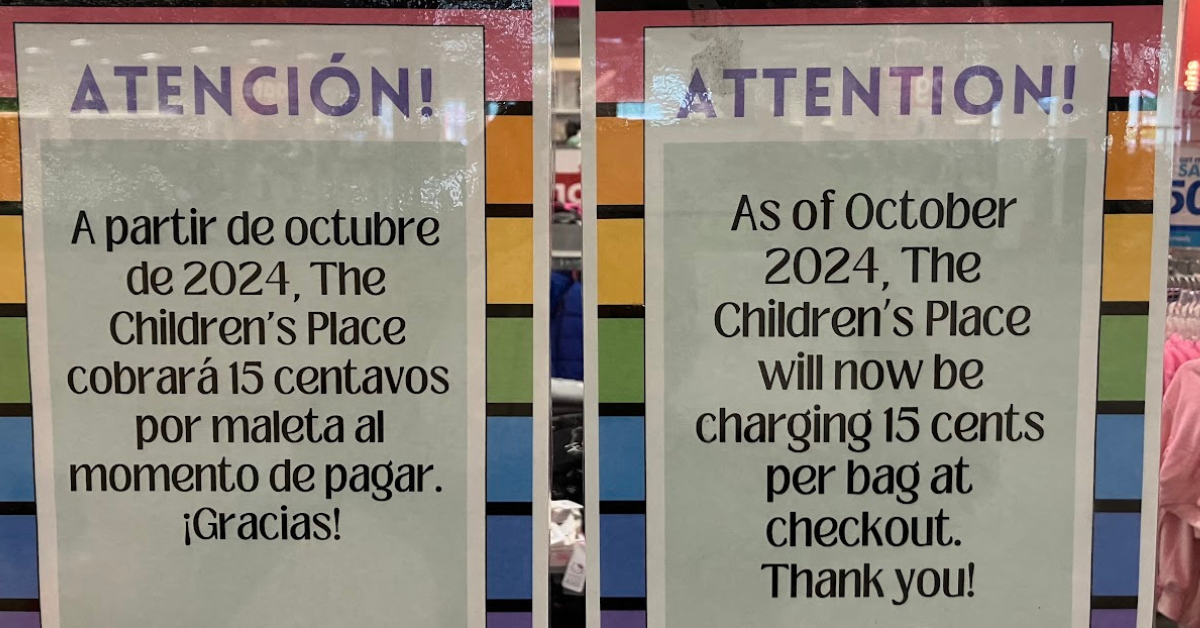 Two signs are side-by-side. The sign on the left is in English and the right is in Spanish. It says "As of October 2024, The Children's Place will now be charging 15 cents per bag at checkout. Thank you!"