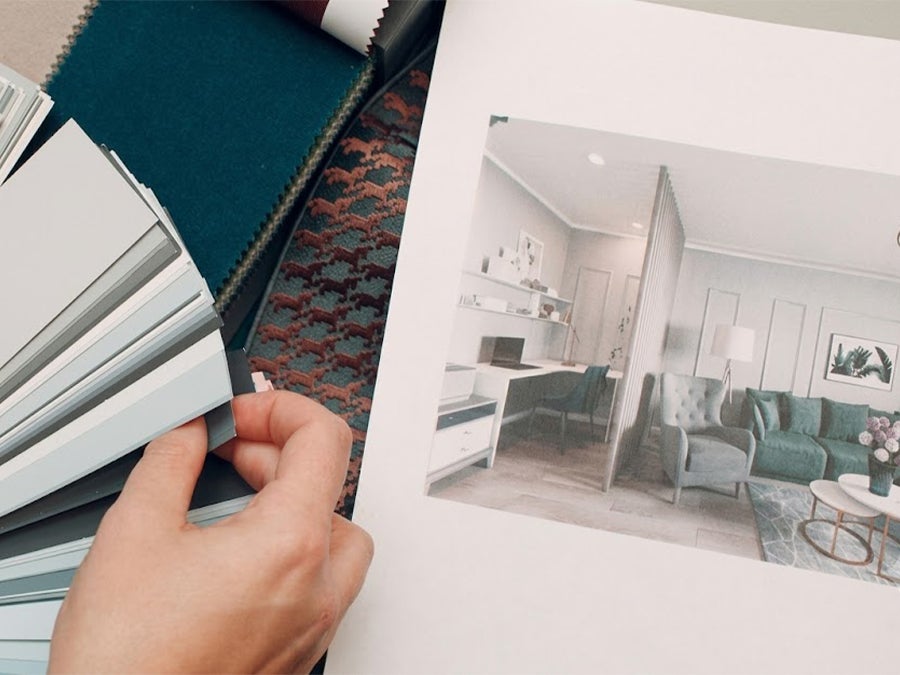 Interior designer holding color swatches and fabric samples next to a room design portfolio.