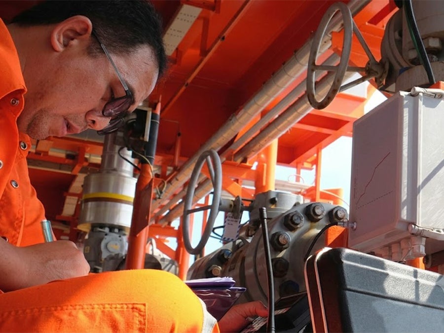 Industrial technician taking notes while inspecting machinery at an advanced manufacturing facility.