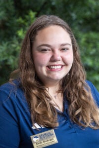 Smiling young woman with long brown hair in a blue polo, wearing a Georgia Southern University badge: Emily Boatright, Southern Ambassador, outdoors.