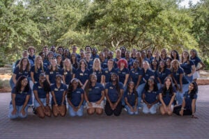 Flight Leaders on the Statesboro Campus pose for a group photo. Trees and shrubbery are in the background. The Flight Leaders are wearing navy blue polo shirts.