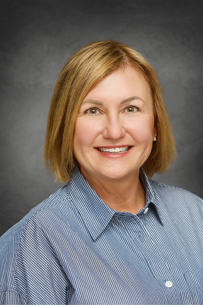Headshot of Dr. Amy Lingo smiling, wearing a blue and white striped collared shirt against a gray neutral background.